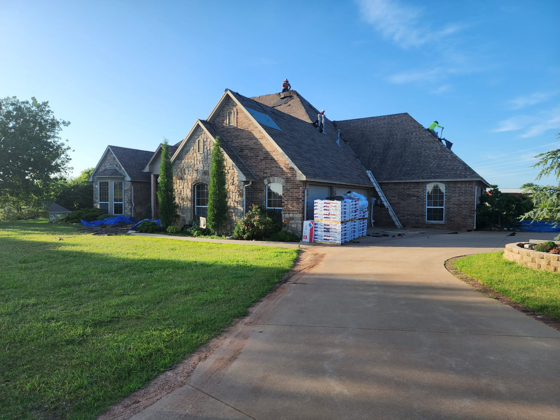 Crew installing new shingles on stone-and-brick Oklahoma home