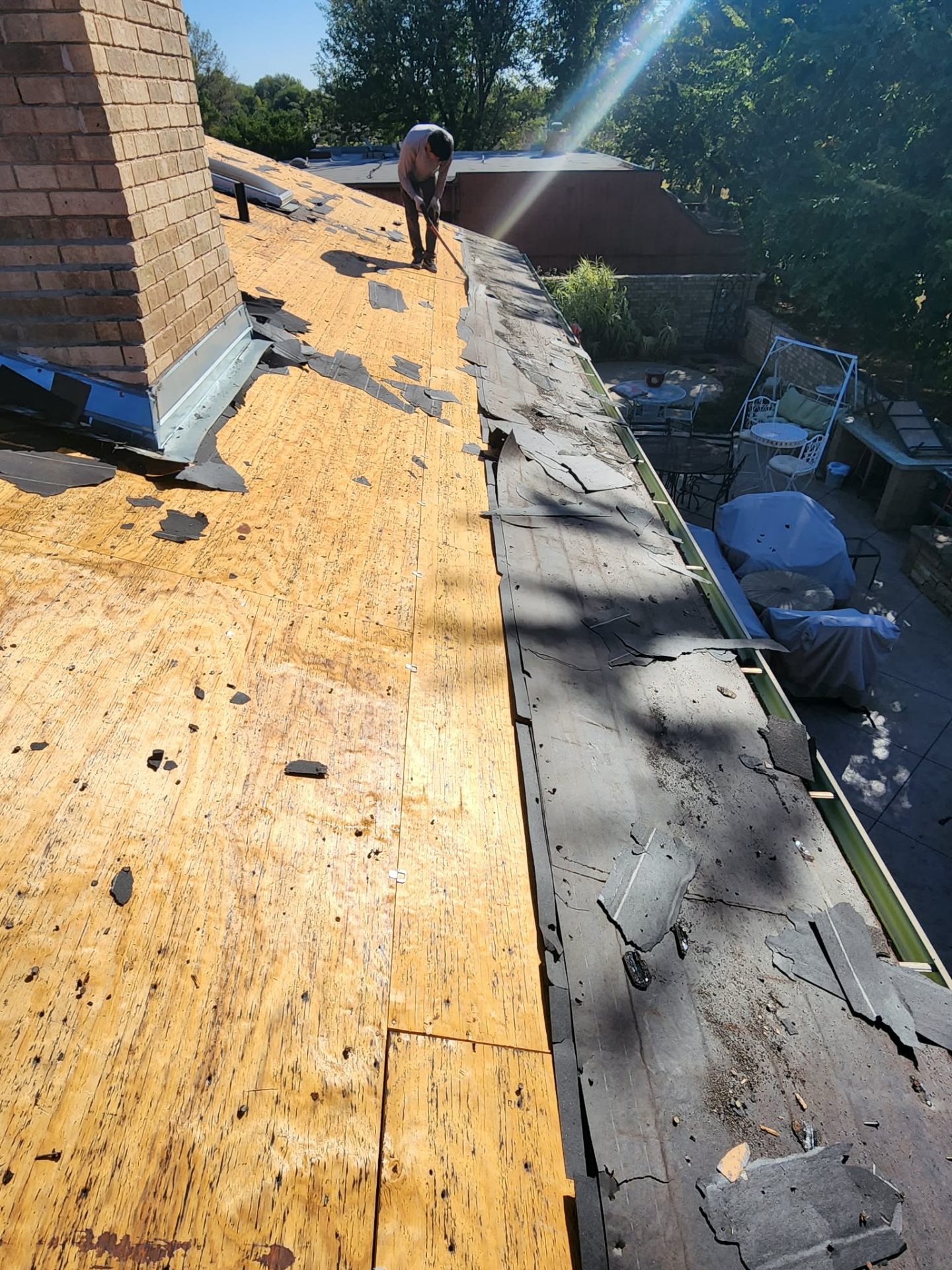 Tear-off in progress around brick chimney — exposed decking