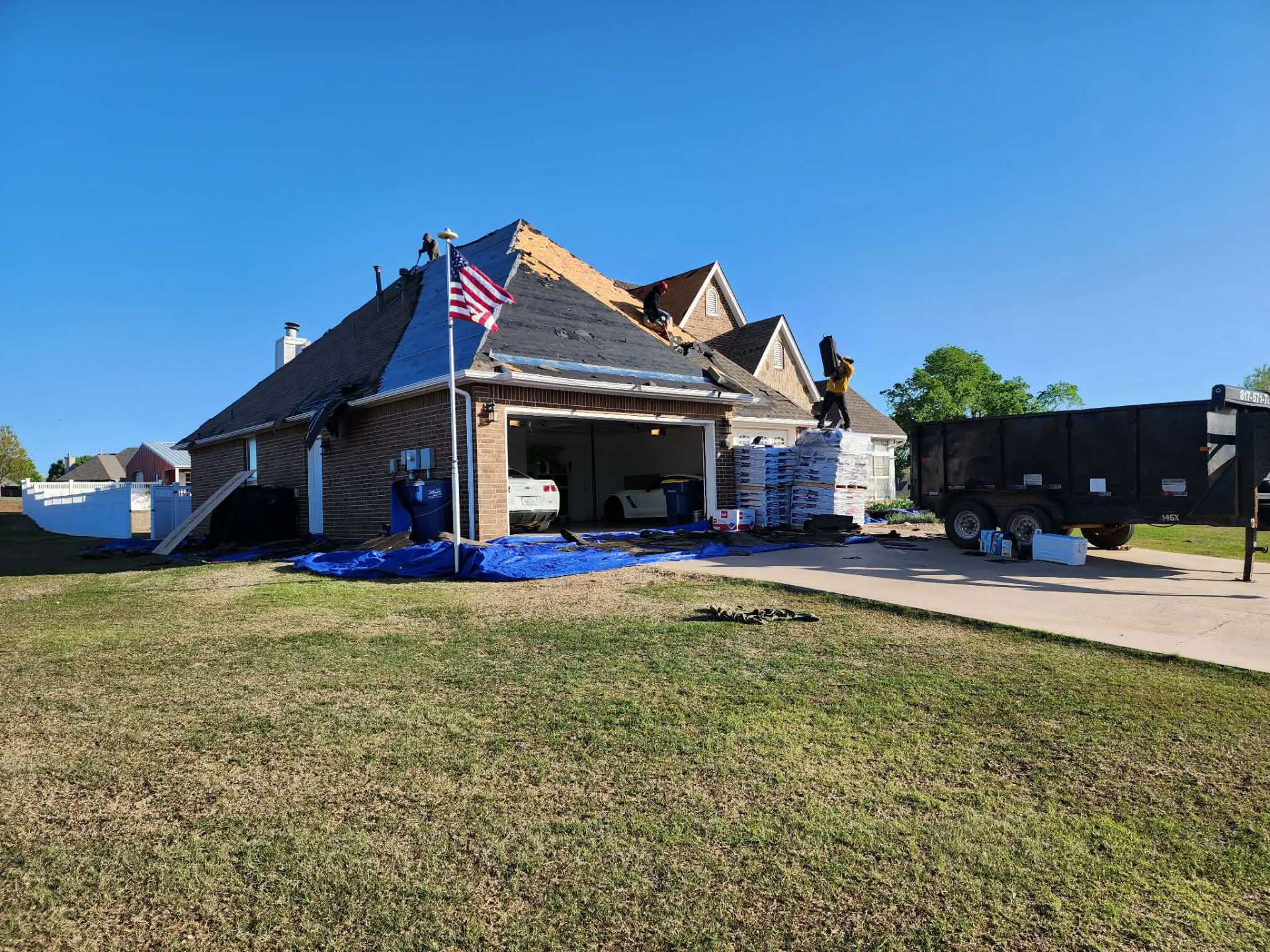 Tear-off day with American flag flying — material staged on driveway