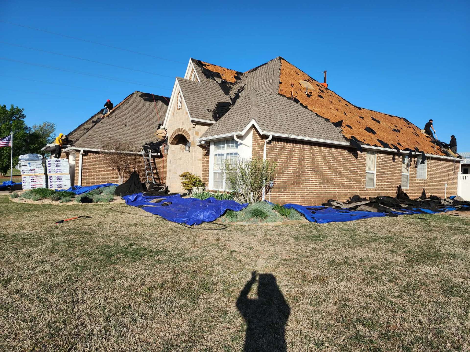 Side view of roof tear-off with pallets of new shingles staged