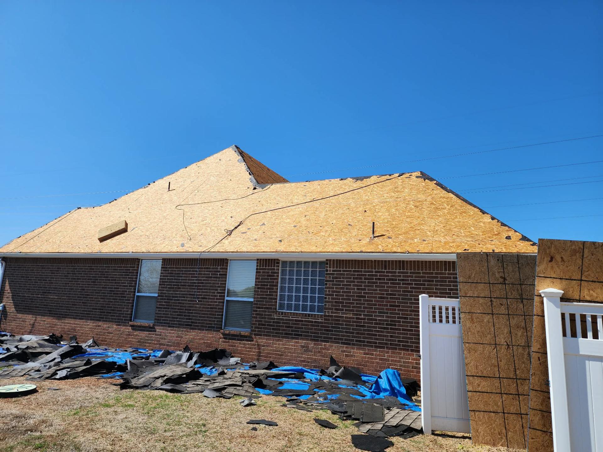 Fresh decking installed on hip roof, old shingles tarped below